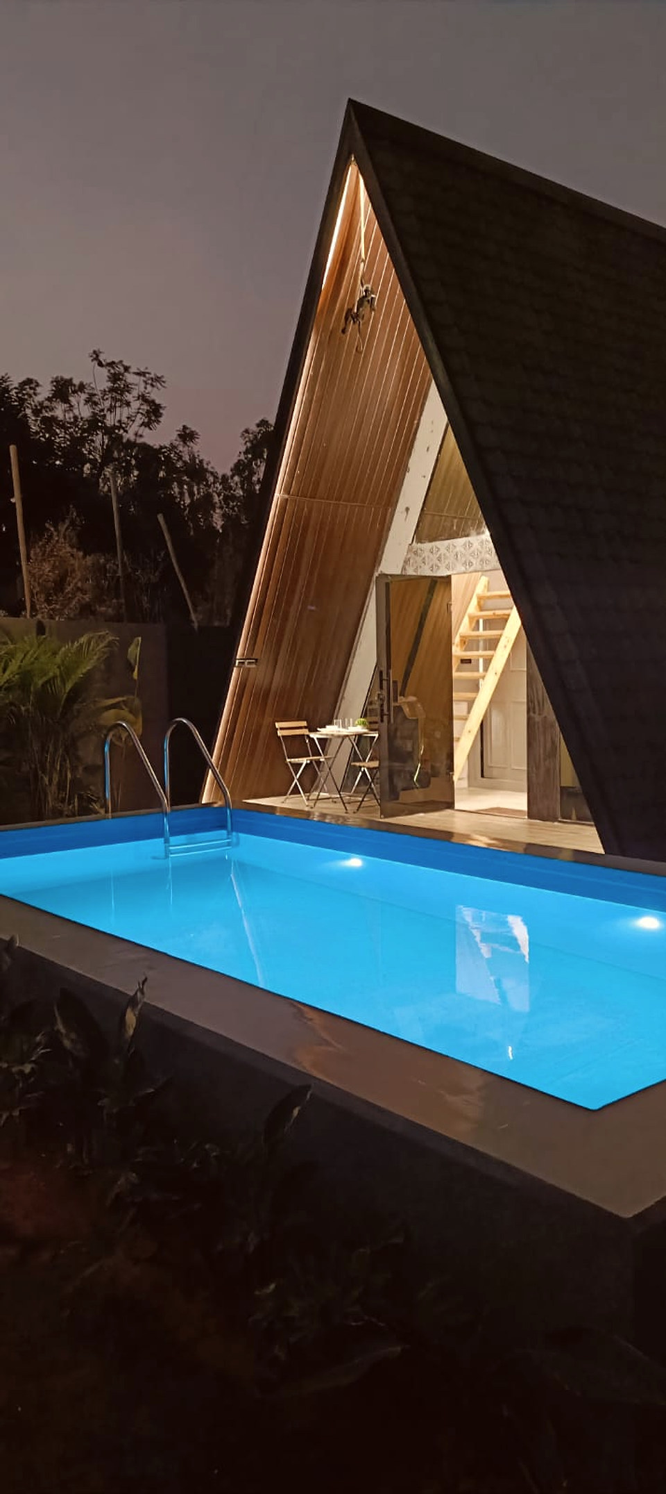 A-frame cottage glowing beside a private illuminated pool